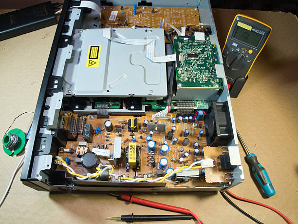 Hands Testing Electronic Circuit Board with Multimeter; Close-up of technician's hands using a multimeter to diagnose or repair complex electronic circuitry inside an open DVD/Blu-ray player or similar device. Hands Testing Electronic Circuit Board with Multimeter; Close-up of technician's hands using a multimeter to diagnose or repair complex electronic circuitry inside an open DVD/Blu-ray player or similar device. open cd player stock pictures, royalty-free photos & images