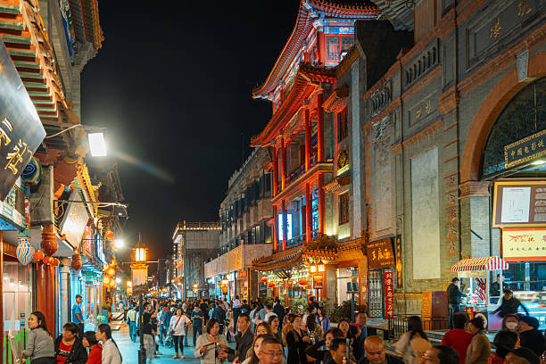 Beijing, China - October 10, 2023:  A vibrant night scene in Beijing featuring a busy street lined with illuminated traditional buildings, colorful lanterns, and crowds exploring shops and food stalls. Cultural, lively, urban atmosphere.