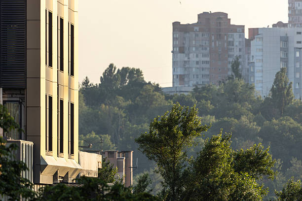 Kyiv, Ukraine. Facade of a modern residential building on Cherepanova Hill with a view of high-rise apartment towers in the background haze. Urban architecture and city development landscape.