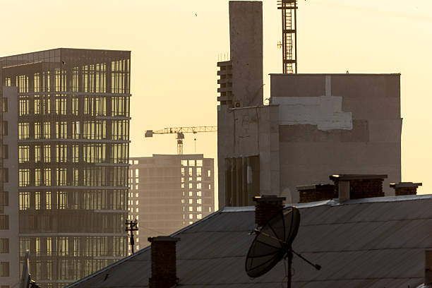 Kyiv, Ukraine. Black satellite dish antenna on an old rooftop with modern high-rise office buildings and construction cranes in the haze. Urban communication and architectural contrast scene.