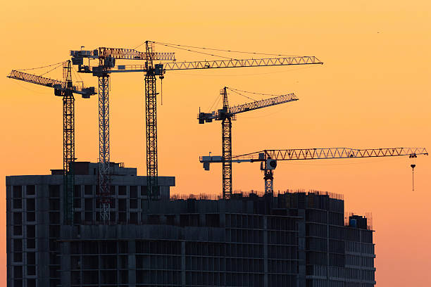 istock Construction cranes silhouettes against orange sunset sky 2254373570