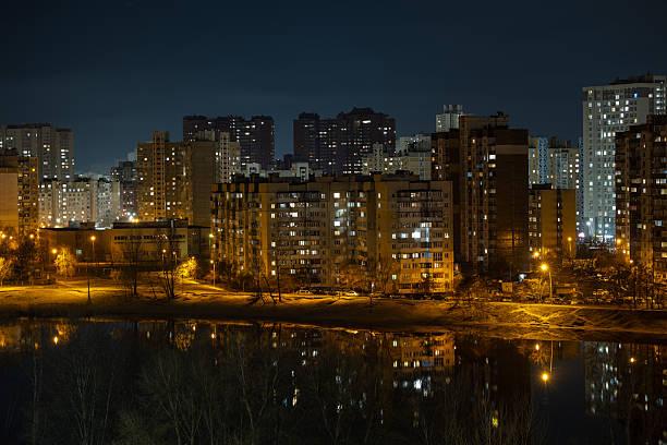 night view of high-rise apartment buildings reflecting in the lake water under a clear starry sky. Bright lights of the sleeping district on the Left Bank city