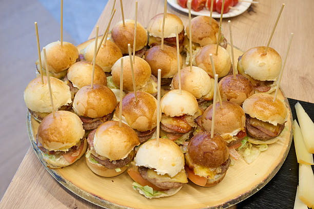 Mini burgers on a rustic wooden platter with toothpicks, presenting a delicious food selection for parties and events