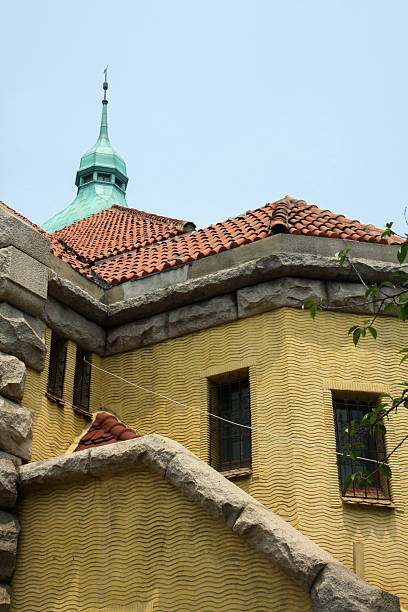 Historic stone building featuring tiled roof and green tower viewed from below. Suitable for architecture, heritage, and travel use.