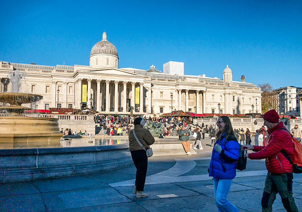 Sightseers enjoying Trafalgar Square in the weeks before Christmas, where the Christmas Market is in full swing in front of the National Gallery.