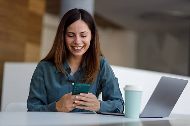 istock Professional woman smiling using phone and laptop, working at office setting during a coffee break 2254386695