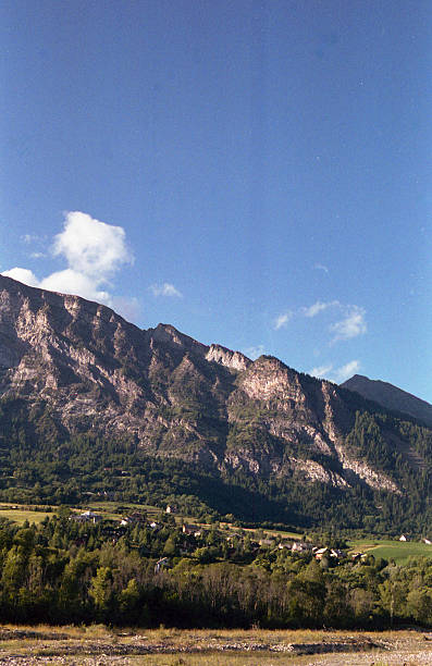 Vertical scanned film photograph of imposing Alpine limestone cliff face with valley village below showing vintage color saturation and film grain