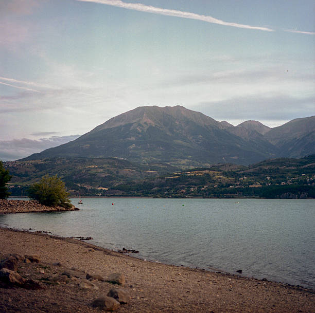 Scanned analog film photograph of mountain lake with distant Alpine peaks and shoreline showing vintage atmospheric tones and subtle grain