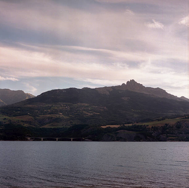 Scanned film photograph of dramatic mountain silhouette across lake with moody atmospheric clouds showing vintage muted tones and grain