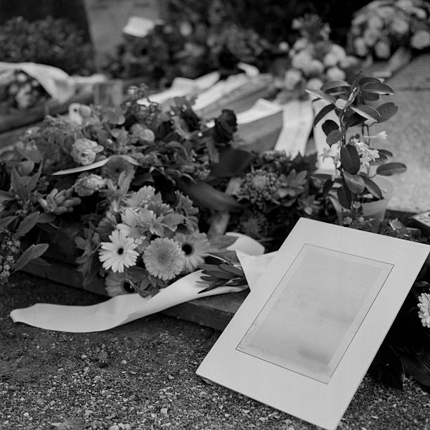 Black and white scanned film close-up of funeral flowers with empty photo frame showing vintage documentary detail and authentic grain
