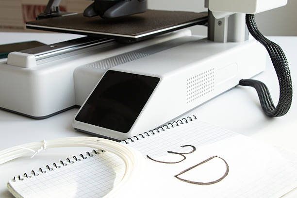 istock A desktop 3D printer with a spool of plastic filament on a white background and a notebook with the text 3D 2254394676