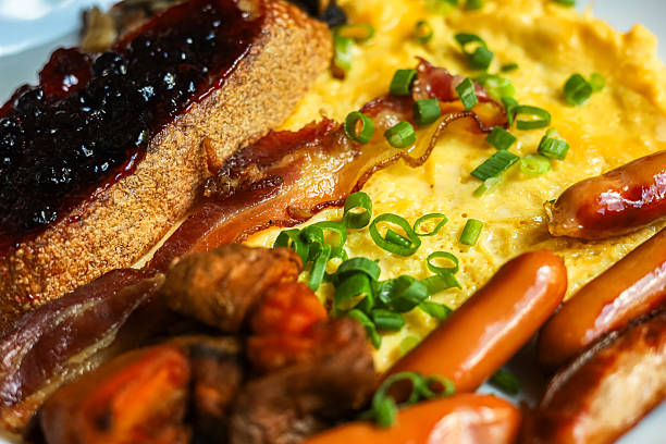Breakfast plate with eggs bacon sausage toast jam and green onions on a white plate