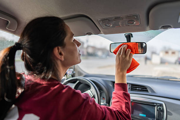 istock Woman Driving Car Inside Clean Windshield Mirror As She Wipes With Orange Cloth 2254399208