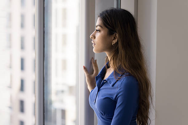 istock Indian woman standing by window, gazing outside with contemplative expression 2254399502