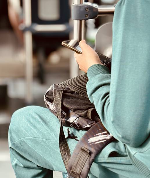 Travel Phone Focus, Modern Digital Connection During Travel, Person Using Smartphone Over Backpack In Transit Environment, Closeup Of Hand With Phone And Teal Sleeve During Quiet Commute