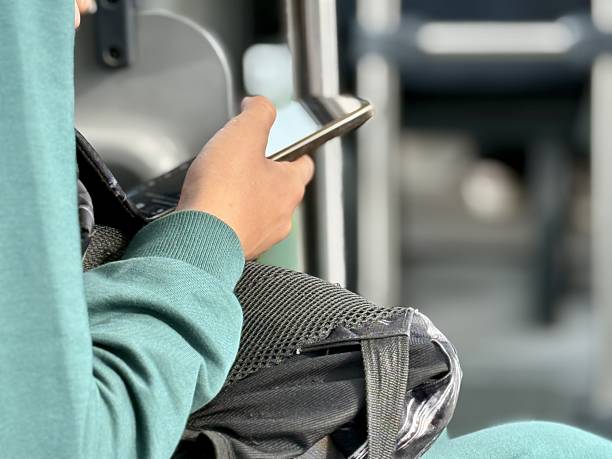 Travel Phone Focus, Modern Digital Connection During Travel, Person Using Smartphone Over Backpack In Transit Environment, Closeup Of Hand With Phone And Teal Sleeve During Quiet Commute