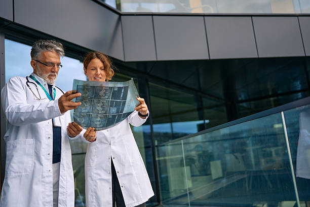 Two doctors, one mature adult man and one mid adult woman, examining x-ray films together on a hospital balcony, discussing patient diagnosis and treatment plans