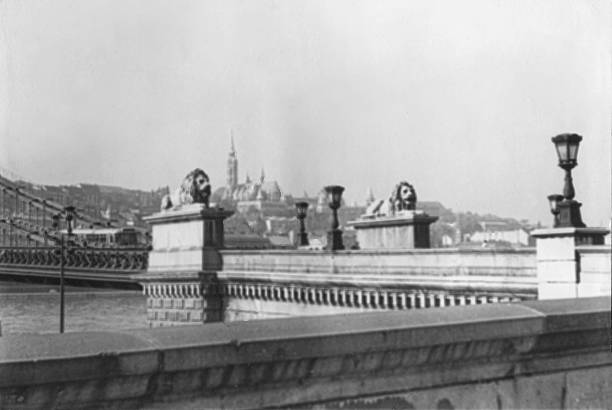 Historic black and white photograph of the Chain Bridge (Széchenyi Lánchíd) spanning the Danube River in Budapest, Hungary, taken in 1969. The bridge connects Buda and Pest and was photographed during the communist era in Hungary, with urban architecture and riverbanks visible in the background. 1969, Széchenyi Lánchíd (Kettingbrug), District V / District I, Boedapest, Hongarije