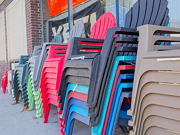 Stacks of brightly coloredplastic Adirondack chairs line up on sidewalk infront of hardware store