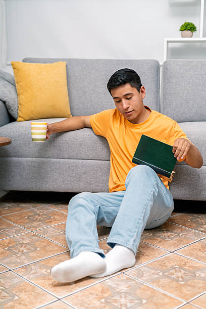 istock Young man relaxing at home reading book with coffee 2254404657