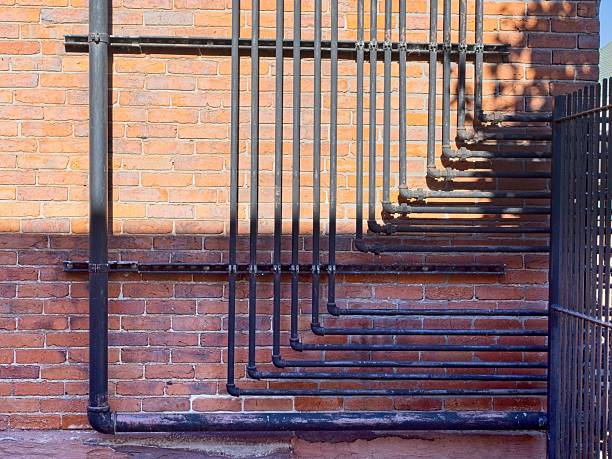 Set of plumbing pipes with elbows mounted to exterior brick wall running horizontally and vertically