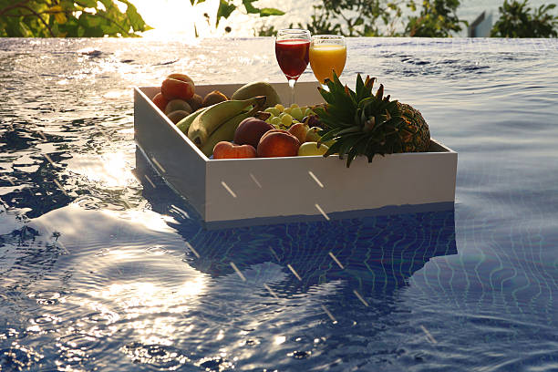 A luxury floating tray filled with fresh fruits drifting in a serene swimming pool, with warm golden light reflecting on the water.