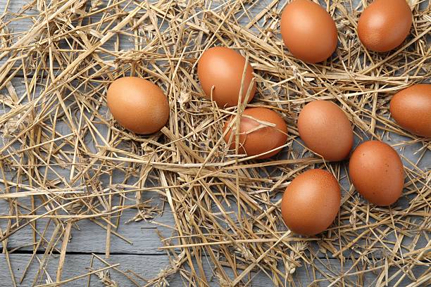 Raw chicken eggs and straw on grey wooden table, flat lay