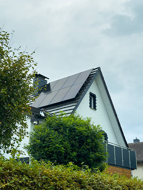 Modern home with solar panels nestled among green trees under a cloudy sky, showcasing a blend of nature and sustainable energy