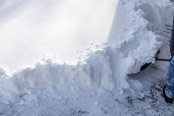 This image shows a partial view of an unrecognizable adult man shoveling deep snow off of a wooden deck, following a blizzard.
