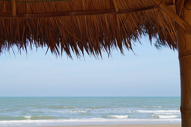 A place for relaxation and recreation on the beach by the sea. A bamboo and thatch roof set against a backdrop of blue sky and turquoise sea.