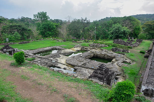 Elevated view of the ancient bathing pools and stone foundations at the Ratu Boko archaeological site, surrounded by green grass and trees under a cloudy sky