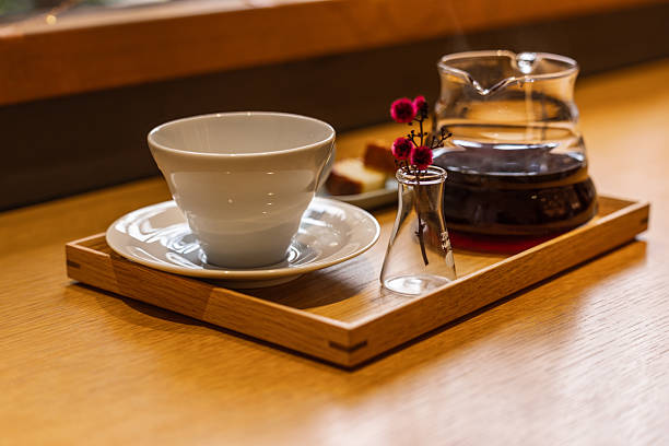 Enjoy a perfect coffee break with a freshly brewed pour-over coffee, steaming in a glass server, alongside a pristine white cup. A unique flask-vase with crimson flowers adds a touch of warmth to this