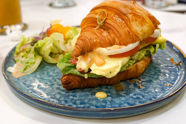 Delicious croissant sandwich filled with scrambled eggs, lettuce, tomato, onion, and creamy dressing, served with a fresh garden salad.