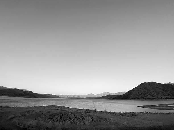 A calm lake lies beneath a vast sky surrounded by rolling hills and distant mountains creating a peaceful scene with smooth water and a sense of quiet solitude