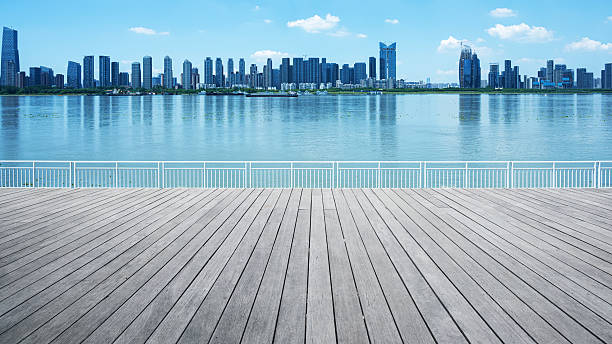 Empty wooden terrace and modern urban waterfront skyline with blue sunny sky and clouds background