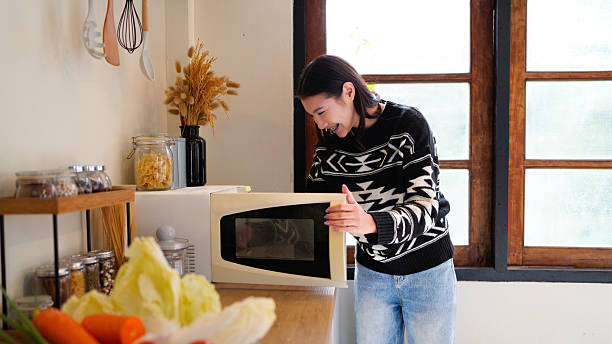 istock side view of smiling woman in shirt using microwave in kitchen 2254441064