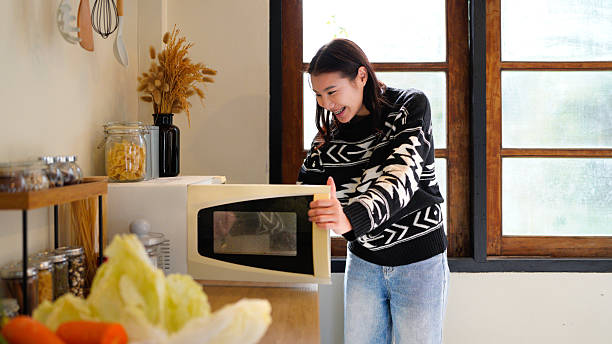 istock side view of smiling woman in shirt using microwave in kitchen 2254441088
