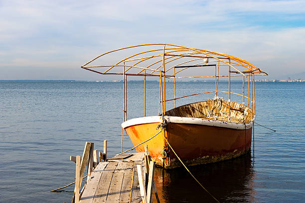 istock Abandoned weathered boat docked at rustic pier—framed by calm water and distant shoreline for nostalgic maritime visuals, decay themes, and contrast between nature and urban structures. 2254441442