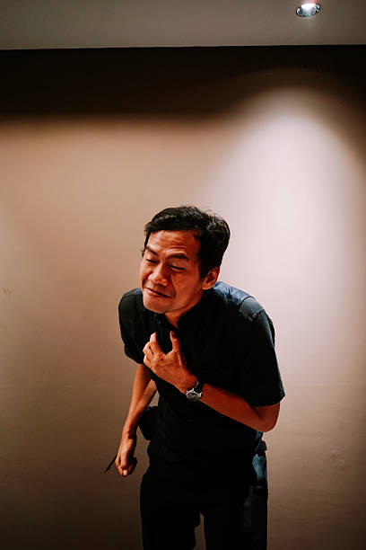 An adult man clutches his chest, grimacing in severe discomfort or pain, possibly a symptom of a heart attack, heartburn, or anxiety attack.