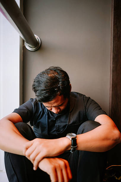 istock Depressed Young Man Sitting Alone with Head Down 2254441506