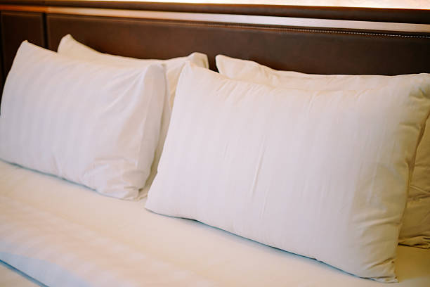 Two soft, clean white pillows resting on a perfectly made bed with crisp sheets and a dark headboard, inviting comfort and a restful night's sleep in a hotel or modern bedroom.