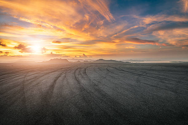 istock Empty asphalt road with tire marks under a dramatic sunset sky with mountains in the background. 2254447716