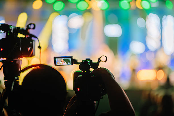 istock Camera operators capturing live performance on stage with colorful lights and blurred audience in the background, showcasing the excitement of a vibrant concert atmosphere 2254451200