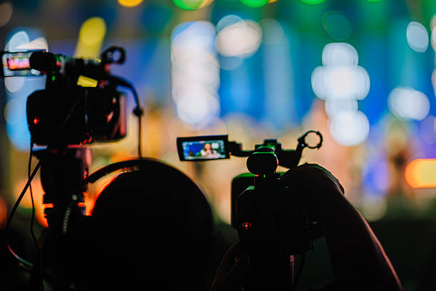 istock Two video cameras positioned in foreground capturing vibrant live performance on stage, with colorful lights and blurred audience in background, showcasing dynamic event atmosphere 2254451226