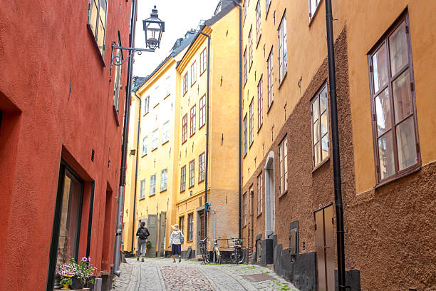 Stockholm, Sweden - June, 18, 2025:  Two Asian tourists walk in the narrow street of Gamla Stan in Stockholm. Bicycles are parked in front the house.