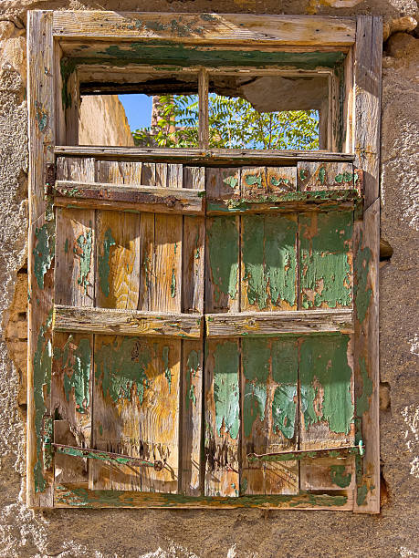 Old wooden window frame and crumbling shutters on an aged stone wall