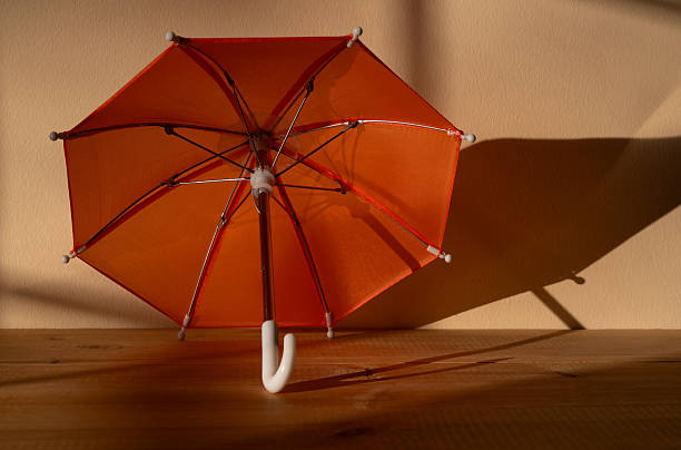 A miniature orange umbrella against a wall with a light and shadow pattern