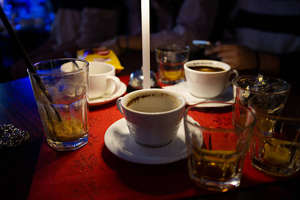 Messy coffee table with cups and glasses on it with people around the table. Cozy dark caffe. People around a coffee table