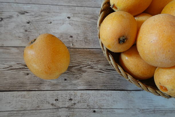 Ripe loquats spilling from a wicker basket onto a weathered wooden table, creating a charming still life