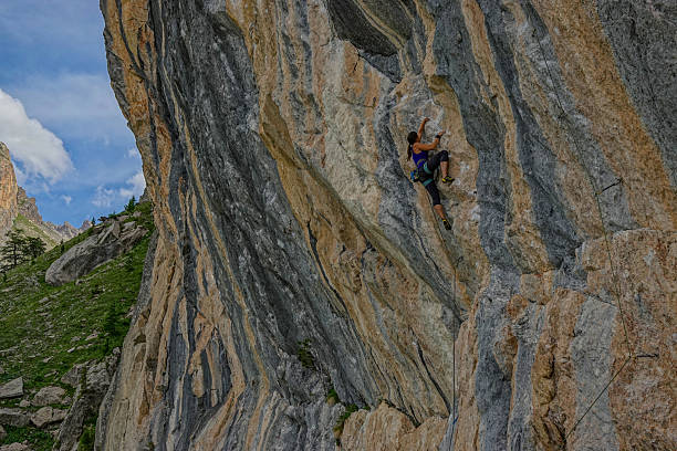 Adventurous climber makes her way up a majestic, streaked rock face with impressive control and poise. Appeal and challenge of outdoor sport climbing in natural alpine environment of the French Alps.